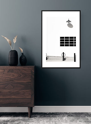Poster of a black lamp on a white wall, framed and displayed above a wooden dresser in a modern room.