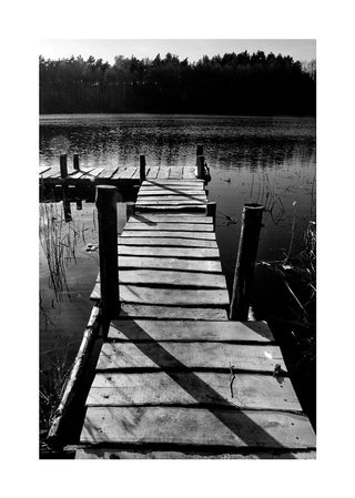 Black and white photo of a wooden jetty extending over a calm lake with trees in the background.