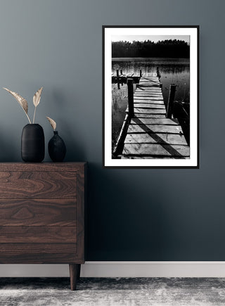 Poster of a wooden lakeside jetty in black and white, hanging on a dark wall above a dresser.