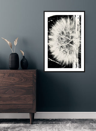 Framed dandelion flower poster hanging on a dark wall above a wooden dresser with minimalist decor.