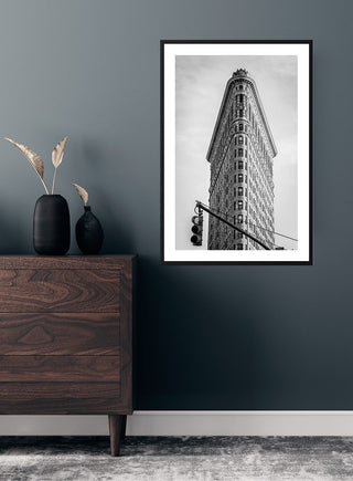 Black and white Flatiron Building poster hanging on a dark wall above a wooden dresser.