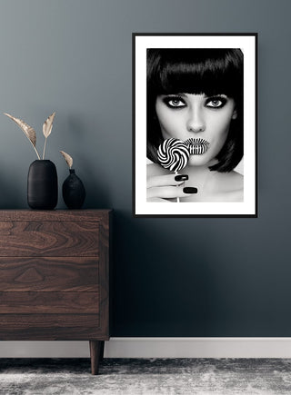 Poster of a woman with matching striped lips and lollipop, displayed in a modern room above a wooden dresser.