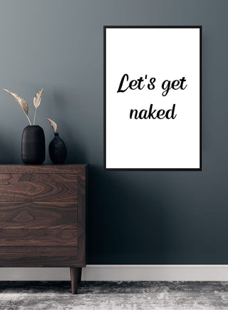 Framed "Let's get naked" poster displayed on a dark wall above a wooden dresser with decorative vases.