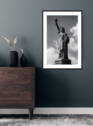 Black and white Statue of Liberty poster hanging on a dark wall above a wooden dresser.