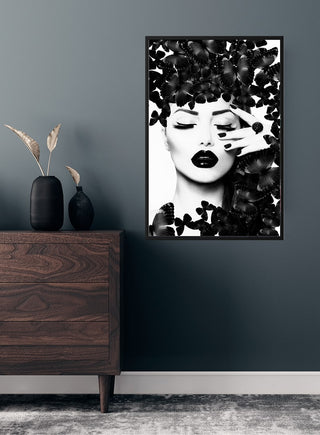 Poster of a woman with black lipstick surrounded by black butterflies, displayed on a dark wall above a wooden dresser.