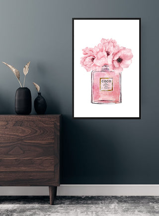 Framed Coco Chanel pink perfume poster with flowers, displayed above a dark wooden dresser in a modern room.