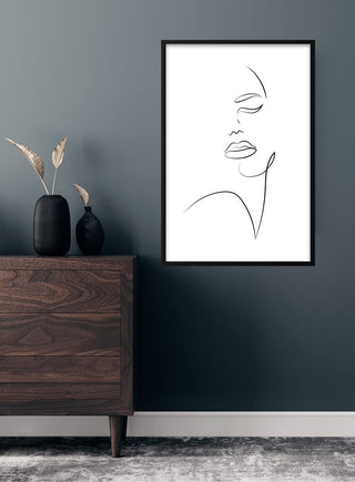 Minimalist line art poster of a woman's face, framed and displayed on a dark wall above a dresser.
