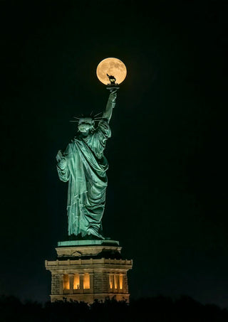 Statue of Liberty at night with a full moon perfectly aligned atop the torch, photo by Hua Zhu.