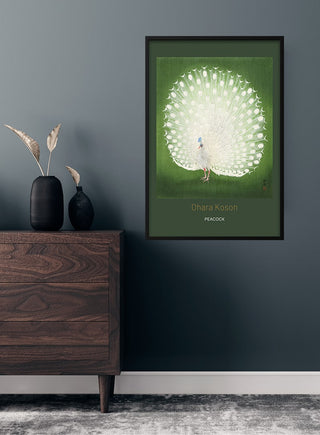 Framed poster of a white peacock by Ohara Koson on a green background, hanging above a wooden dresser.
