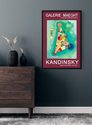 Framed Wassily Kandinsky Gallerie Maeght poster on a dark wall above a wooden dresser with vases.