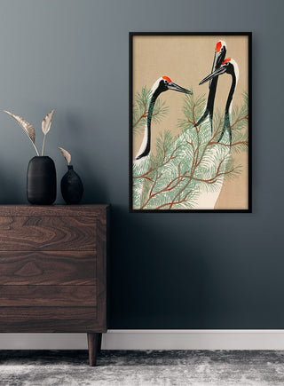 Framed Traner fra Momoyogusa 1909 poster featuring elegant cranes among pine branches on a wall above a dresser.
