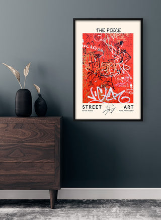 Framed "Street Art - The Piece no. 2" poster with red graffiti, displayed on a dark wall above a wooden dresser.