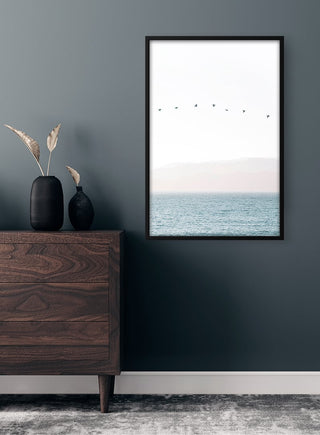 Framed "Birds in a Straight Line" plakat on wall above wooden dresser, minimalist room decor.