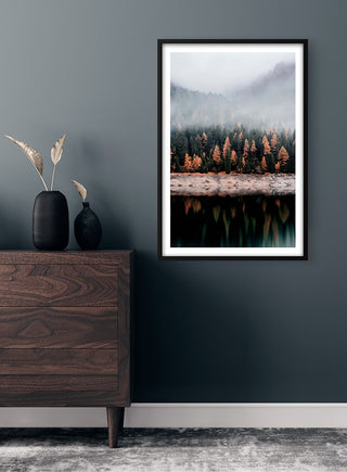 Framed poster of autumn trees by a lake with misty mountains, displayed above a wooden dresser.