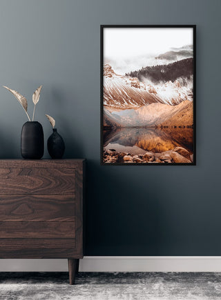 Framed nature poster of a mountain and lake, displayed above a wooden dresser in a modern room.