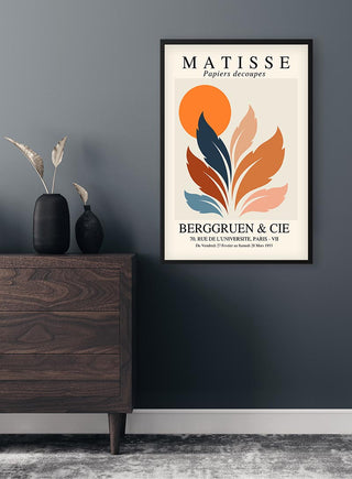 Framed Matisse inspired poster with abstract orange sun and leaf shapes, hanging on a dark wall above a dresser.