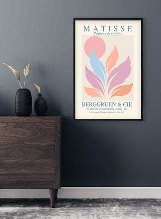 Framed Matisse Inspired Pink Sun Plakat with abstract pastel shapes hanging on a dark wall above a wooden dresser.
