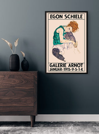 Framed Egon Schiele Galerie Arnot 1915 poster with a seated woman, displayed on a dark wall above a dresser.