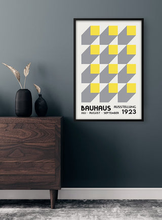 Framed Bauhaus Ausstellung Yellow 1923 Plakat with geometric pattern, displayed on a modern wall above a wooden dresser.