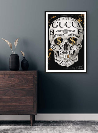 Poster of a skull made from luxury brand logos hangs on a modern wall above a wooden dresser with vases.
