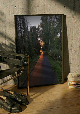 The Amber Forest Path by Bora Kőhalmi in a black frame leaning against a concrete wall by a steel chair