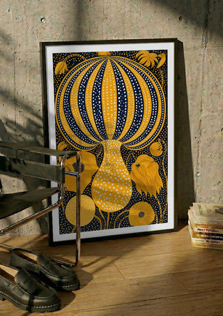 Yellow Dotted Pumpkin by Yokohama in a black frame leaning against a concrete wall by a steel chair