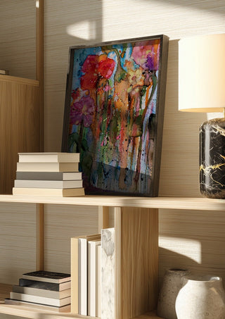 riot garden by hazelart in a dark frame on a wooden shelf beside books and a lamp