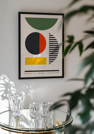 Bauhaus Shapes by Neil Stevens in a black frame above a glass table with crystal glassware