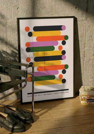 Bauhaus Stacks by Neil Stevens in a black frame leaning against a concrete wall by a steel chair