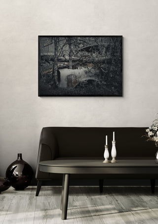 Decay (1) by Lone Gjessing in a black frame on a pale wall above a dark sofa with candlesticks