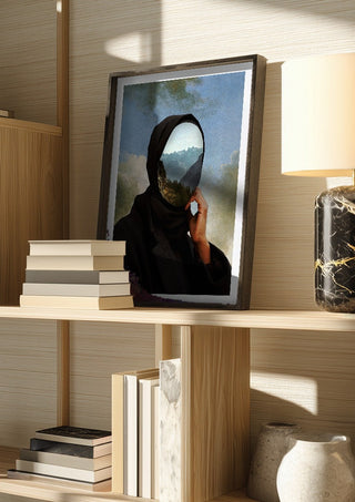 The Mountain Within by Fran Rodriguez in a dark frame on a wooden shelf beside books and a lamp