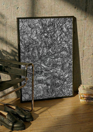 Resized Imagination by Priit Ruttas in a black frame leaning against a concrete wall by a steel chair