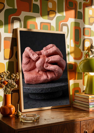 Hold Me - Terracotta Hands by Ammar in a wooden frame on a sideboard against retro patterned wallpaper