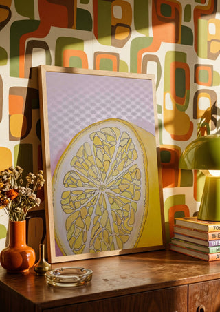 Half Lemon by L.OE. Art in a wooden frame on a sideboard against retro patterned wallpaper