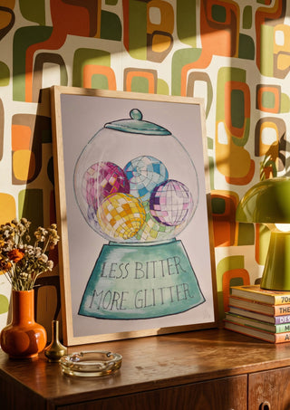 Less Bitter More Glitter by L.OE. Art in a wooden frame on a sideboard against retro patterned wallpaper
