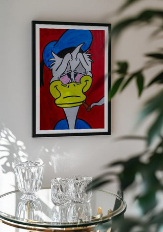 Duck in Dystopia by Bibi in a black frame above a glass table with crystal glassware