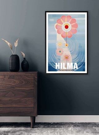 Framed Hilma No 04 - Tara Green print with abstract pink flower, hanging on a blue wall above a wooden dresser.