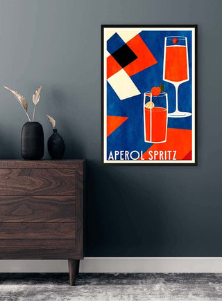Framed Aperol Spritz art print featuring two red cocktails, modern geometric design on a dark wall above a wooden dresser.