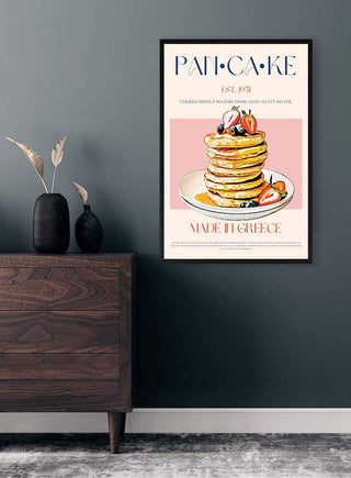 Framed pancake poster with fruit toppings displayed above a wooden cabinet against a gray wall.