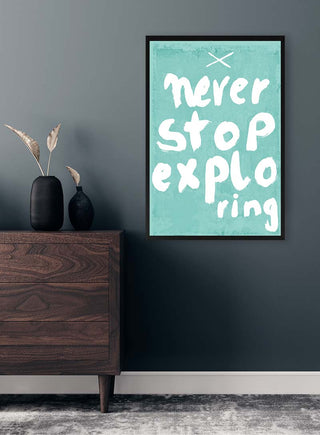 Framed "Never Stop Exploring" print on a teal background, displayed above a dresser in a modern room.