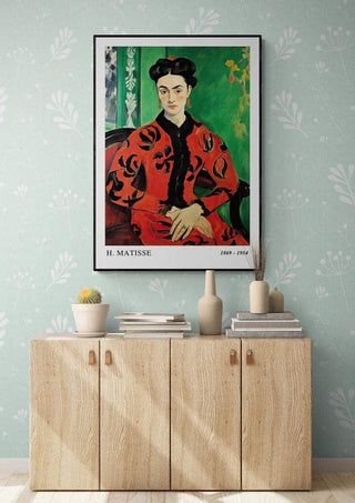 Framed Matisse Madame Rouge poster displayed above a light wood cabinet in a modern, decorated room.