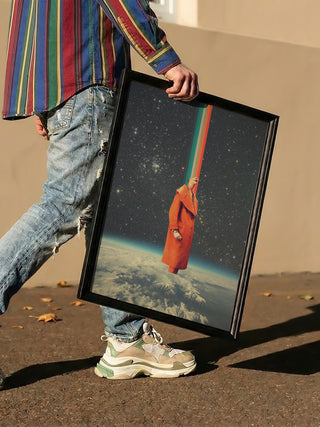 Person holding a framed Spacecolor - Frank Moth artwork featuring an astronaut and colorful beam over Earth.