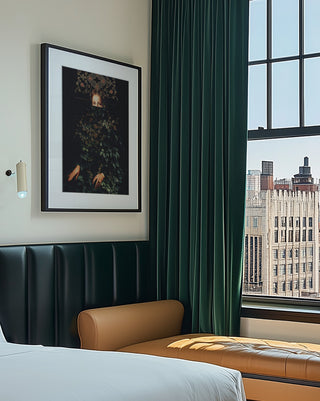 Patience II by Frank Moth framed on a wall above a bed, with city buildings visible through the window nearby.