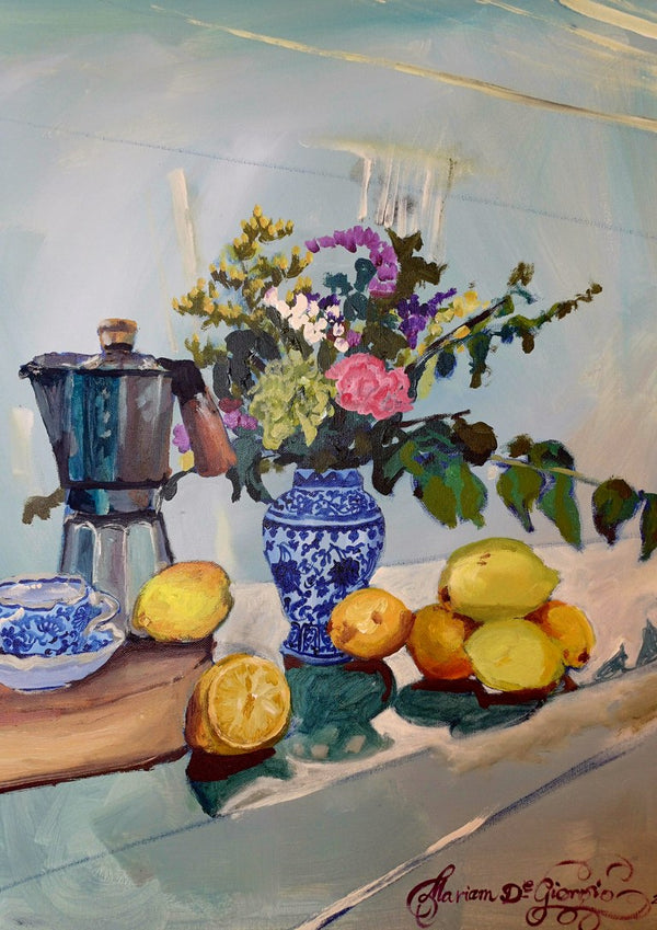 Morning coffee by Mariam De Giorgio — a steel espresso pot, lemons and a blue-and-white vase of flowers on a pale table.