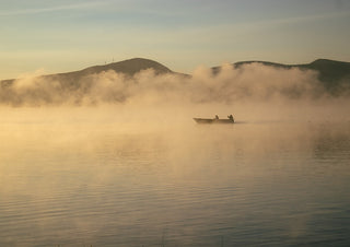 Fishermen Of Naivasha. (three) by Gloria Mwivanda - a small boat in golden mist on a lake at dawn