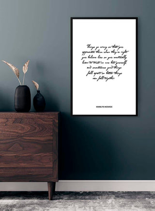 Framed Marilyn Monroe quote poster hanging above a wooden dresser with black vase and dried plants.