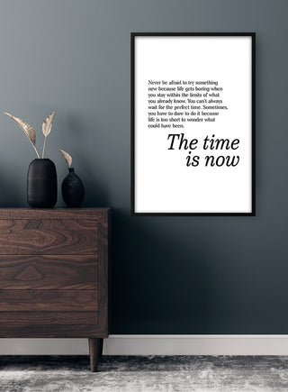 Minimalist "The Time Is Now" poster on wall above mid-century dresser with black vase and dried grasses.