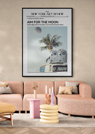 Framed "The Moon - Art Review" poster above a modern pink sofa in a stylish living room setting.