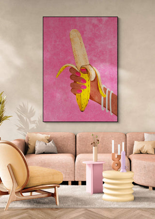 Large artwork of a hand holding a peeled banana on pink background, displayed in a modern living room.
