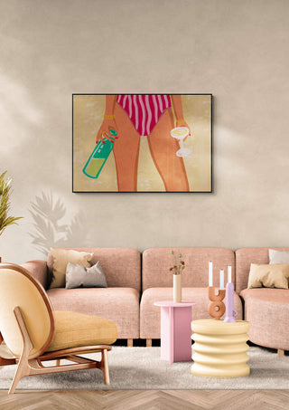 Framed art of a girl in striped swimwear holding wine and bottle, hanging above a modern pink-toned sofa.